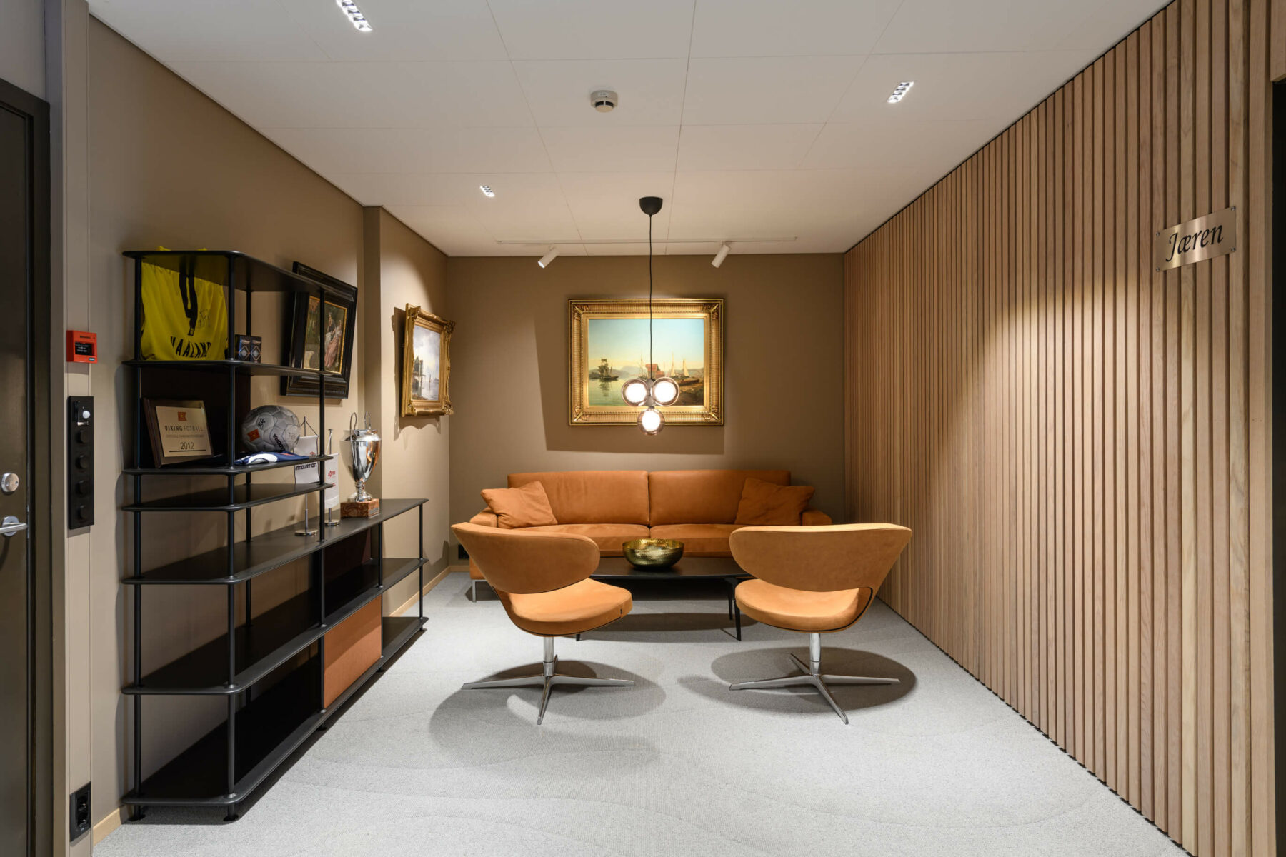 Venterom med trepanel på vegg og to oransje stoler og en oransje sofa