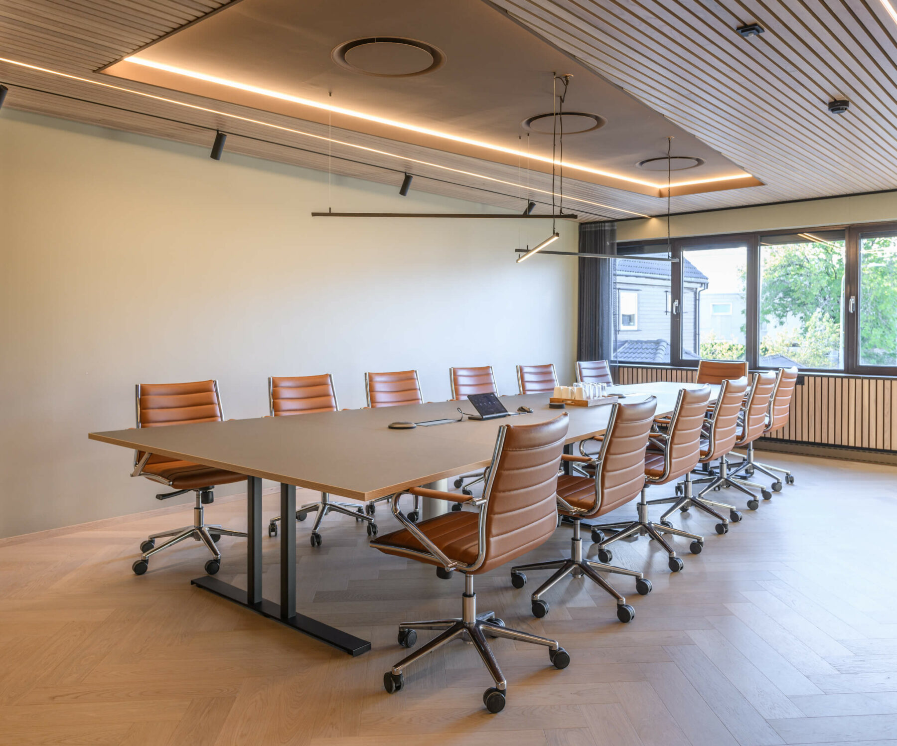 Møterom med et langbord med skinnstoler på hjul og et vindu i enden