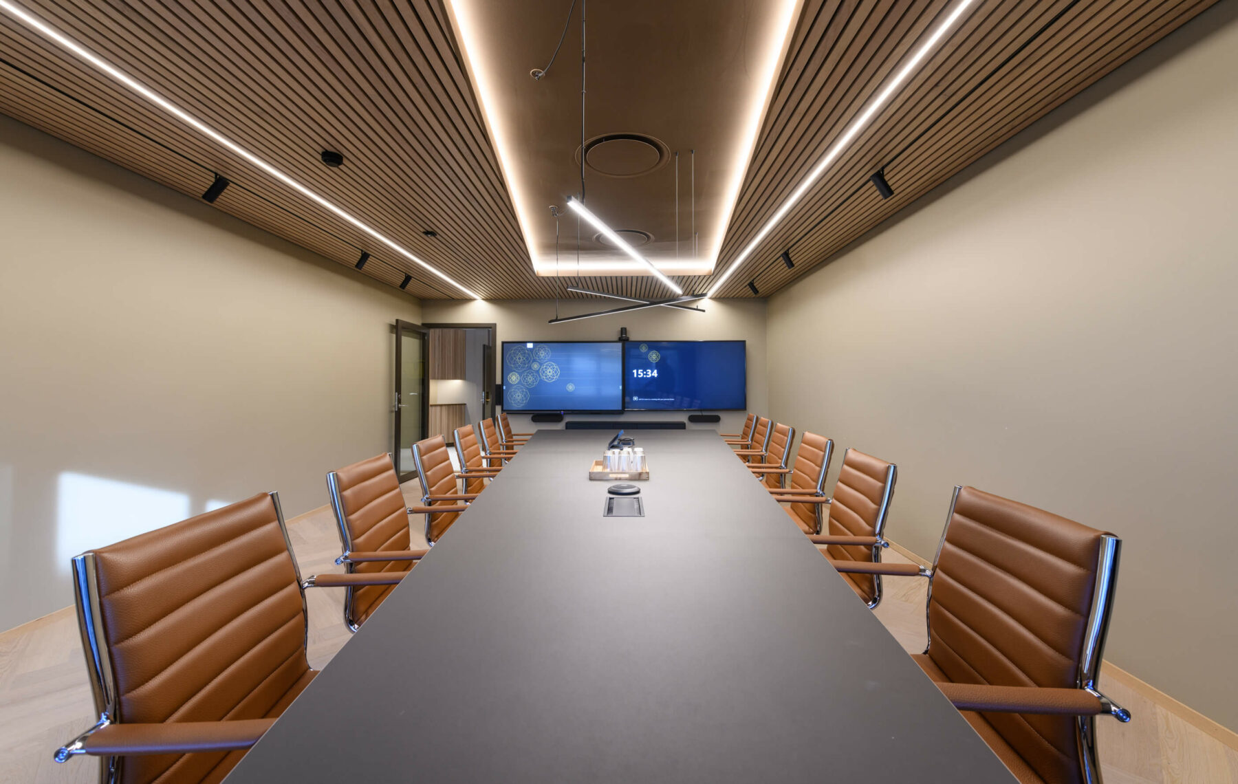 Møterom med en gjeng med brune skinnstoler og to store skjermer på veggen