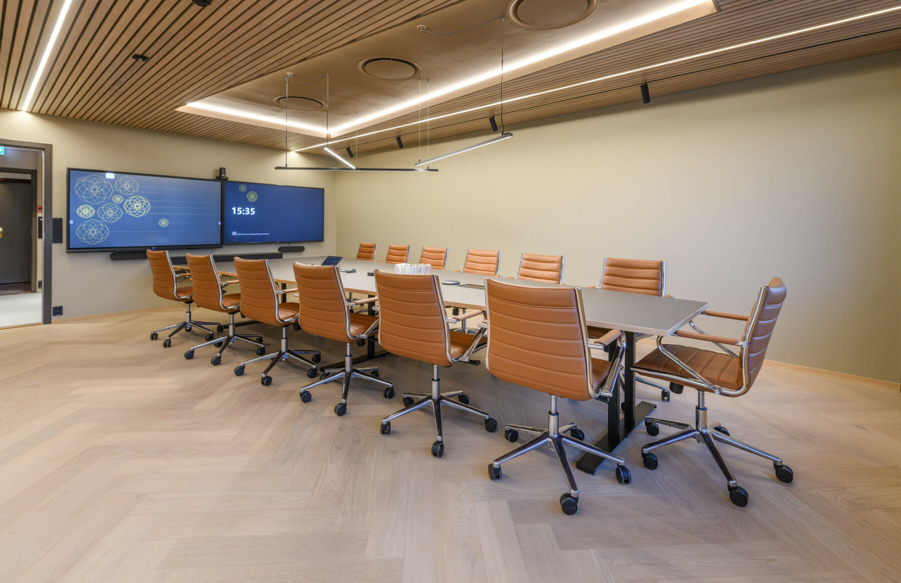 Møterom med brune skinnstoler på hjul og to store skjermer