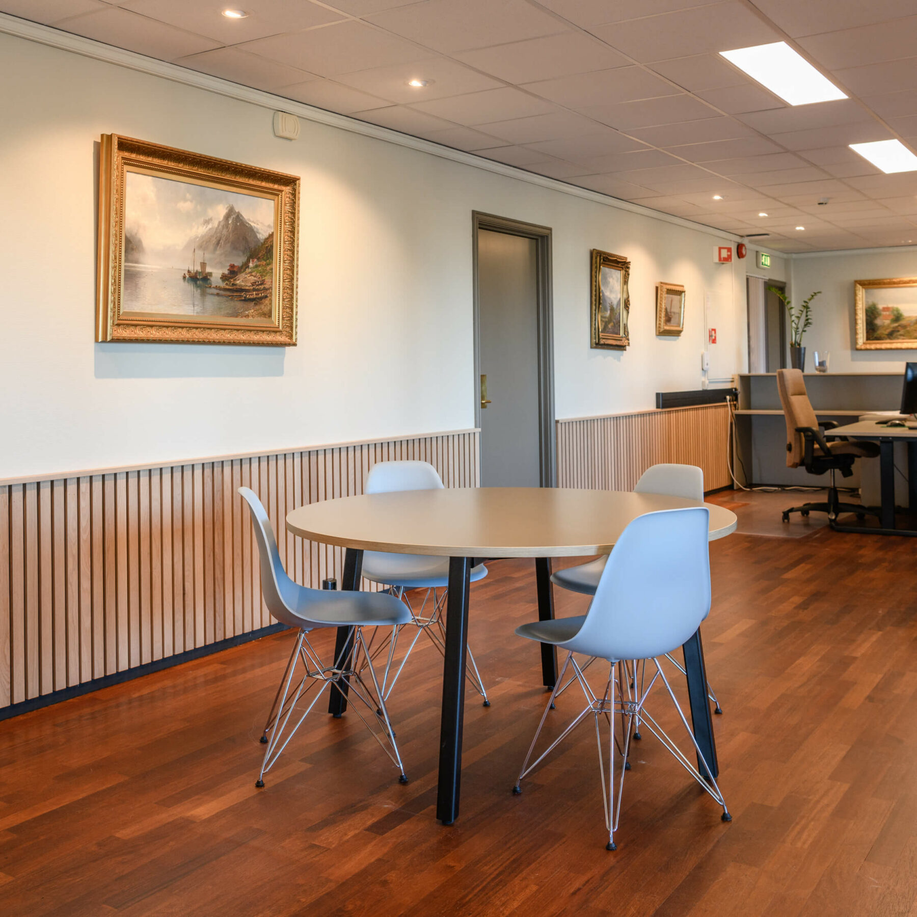 Resepsjon med trepanel på vegg og fire hvite stoler rundt et bord og en resepsjonsdisk i bakgrunnen