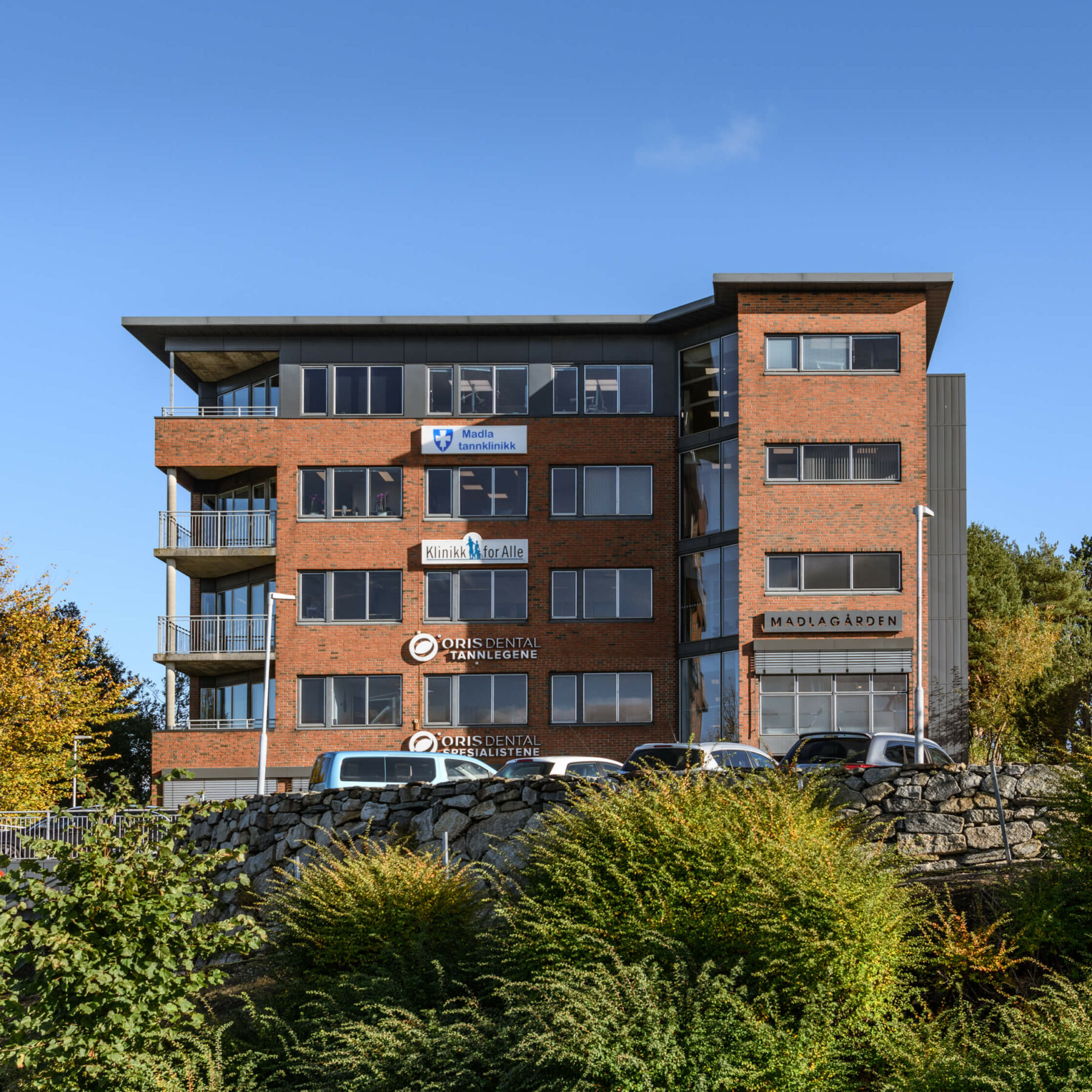 bygning fasadebilde med blå og skyfri himmel og grønne busker foran