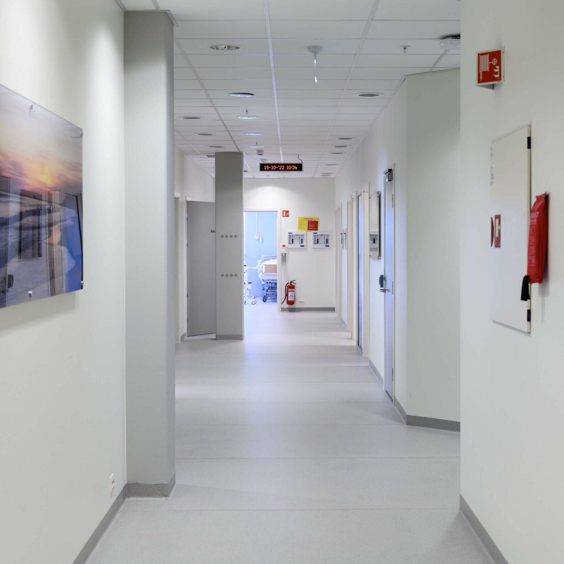 Hvit gang med en synlig sykehusseng inne på et rom i enden av gangen